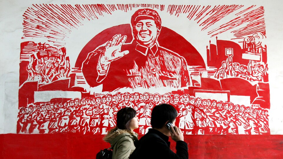 Deux personnes passent devant l'affiche qui représente le leader Mao Zedong souriant devant une foule de travailleurs.
