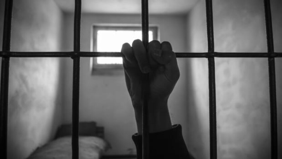 Une main tient un barreau dans une prison.