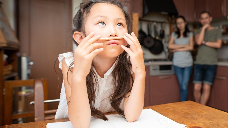 Une fillette attablée joue avec son crayon au lieu d'étudier