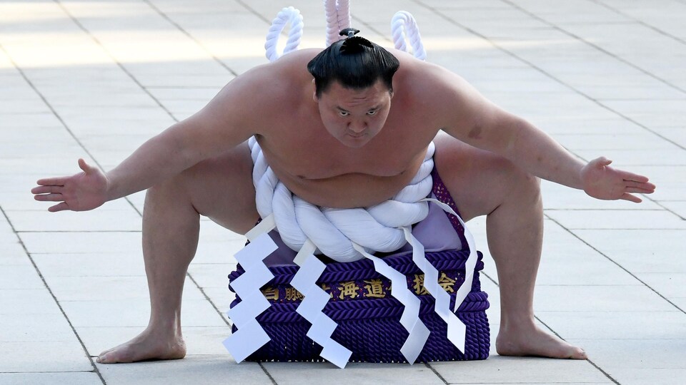 Un lutteur de sumo fait une sorte de salut en ouvrant ses bras.