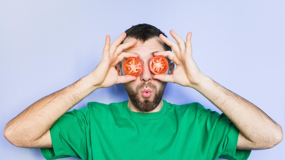Un jeune homme tient des rondelles de tomates devant ses yeux.