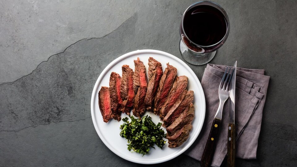 Vue aérienne d'un steak de bœuf coupé en tranches dans une assiette avec un verre de vin rouge. 