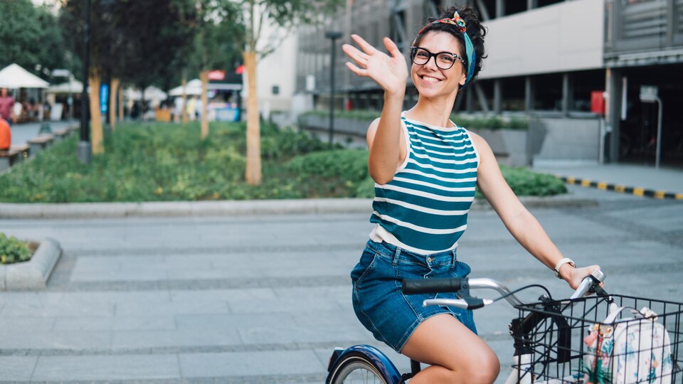 Une jeune femme à vélo sourit en agitant la main.