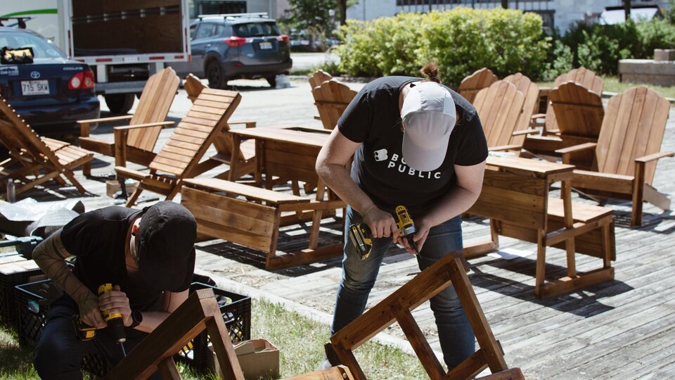 Deux hommes construisent des bancs publics dans une place urbaine.