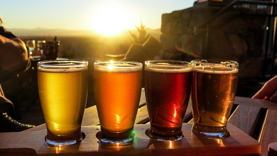 Quatre verres de bière en palette de dégustation sur fond de coucher de soleil.