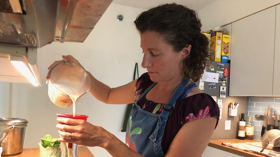 Une femme est dans une cuisine et transverse du lait d'une tasse à mesurer à une carafe en verre.