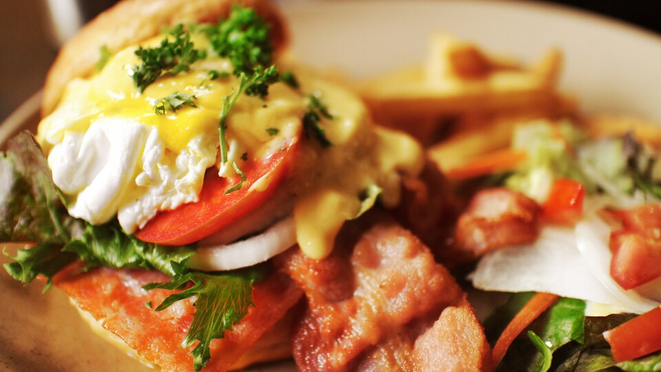 Des oeufs sur un muffin anglais avec de la sauce et du bacon