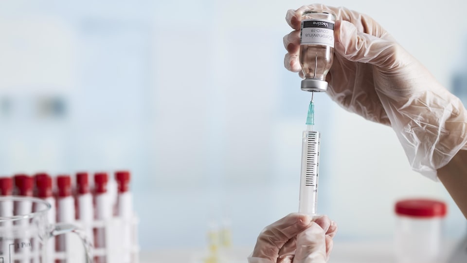 Une seringue et un vaccin se font manipuler en laboratoire.