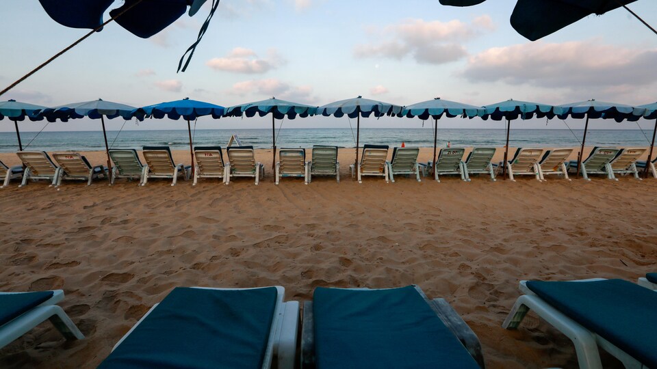 Des chaises longues vides sur une plage déserte.