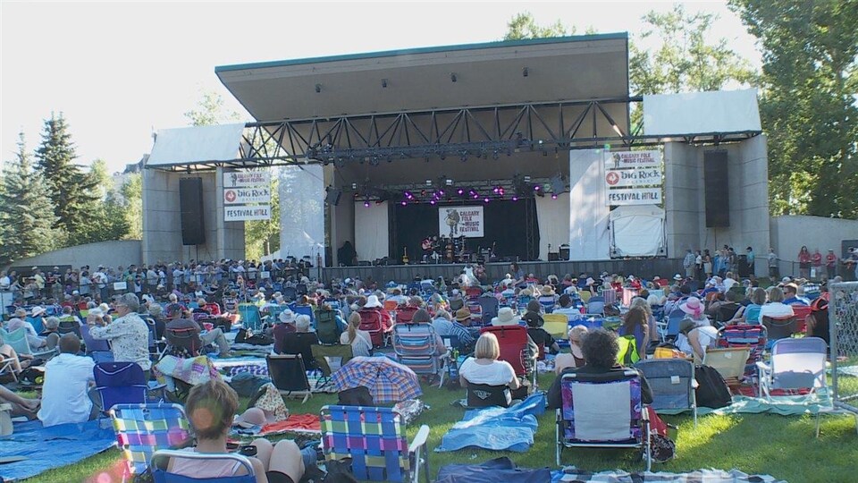 Des gens sont assis sur la pelouse devant une scène au festival folk de Calgary.