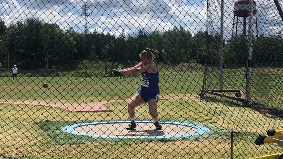 La jeune athlète Camille Desjardins en train de faire un lancer du marteau, sur un terrain dehors.