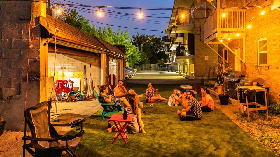 Un groupe d'adultes et d'enfants assis sur une pelouse verte alors que la nuit tombe et que la ruelle est illuminée.