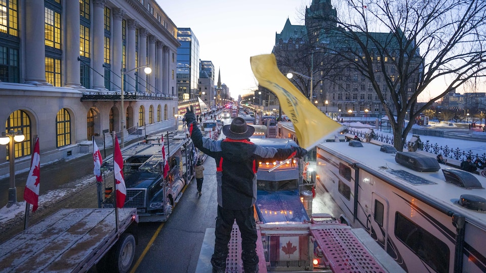 A man waves a flag in front of heavy vehicles on Parliament Hill in Ottawa.