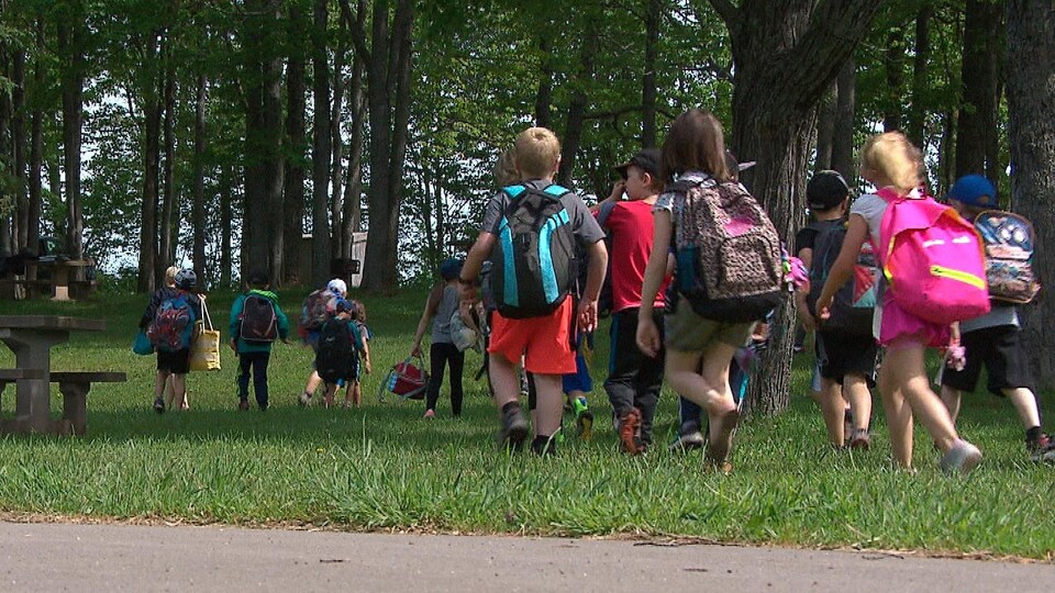 Des enfants marchent dans un parc avec leurs sacs à dos.