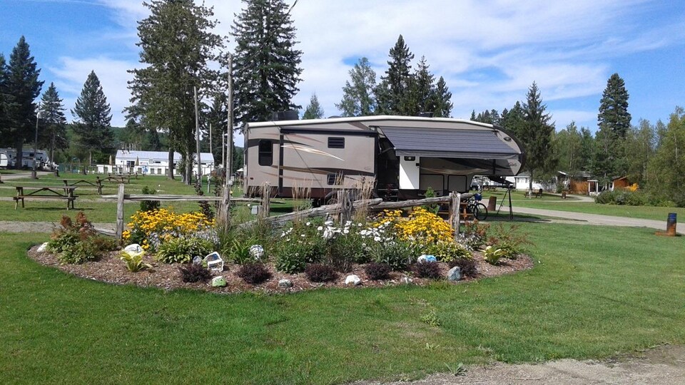 Une tente roulotte se trouve sur un terrain de camping, ainsi que des petites maisons en arrière-plan.