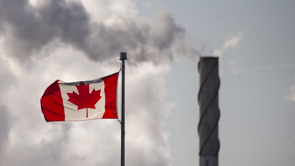 Un drapeau canadien avec, en arrière-plan, de la fumée qui sort d'une cheminée.