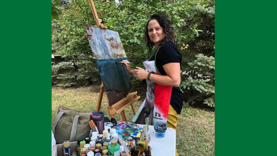 Peintre de sexe féminin au regard perçant et sourire de Joconde avec son chevalet et ses tubes de peinture dans un sous-bois ou il fait bon vivre.