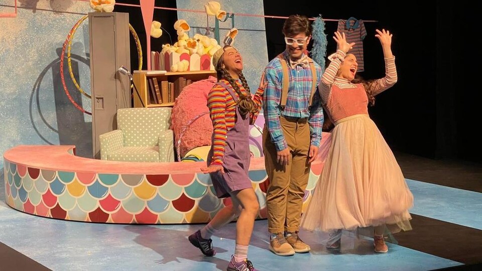 Trois personnes se trouvent sur scène avec des costumes colorés.