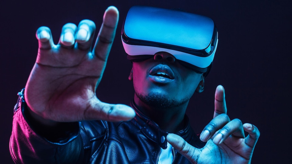 Un jeune homme porte des lunettes de réalité virtuelle avec les mains vers le haut, isolé sur fond sombre. 