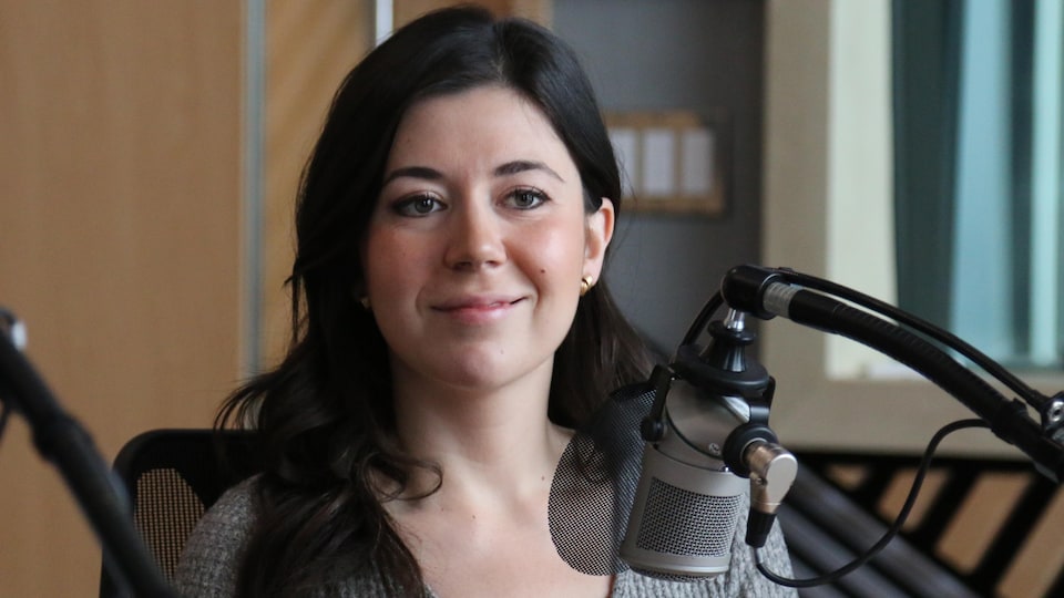 Une femme sourit devant un micro dans un studio de radio. 