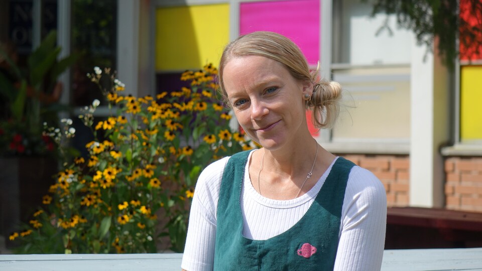 L'autrice devant des fleurs et un fond coloré extérieur sourit.