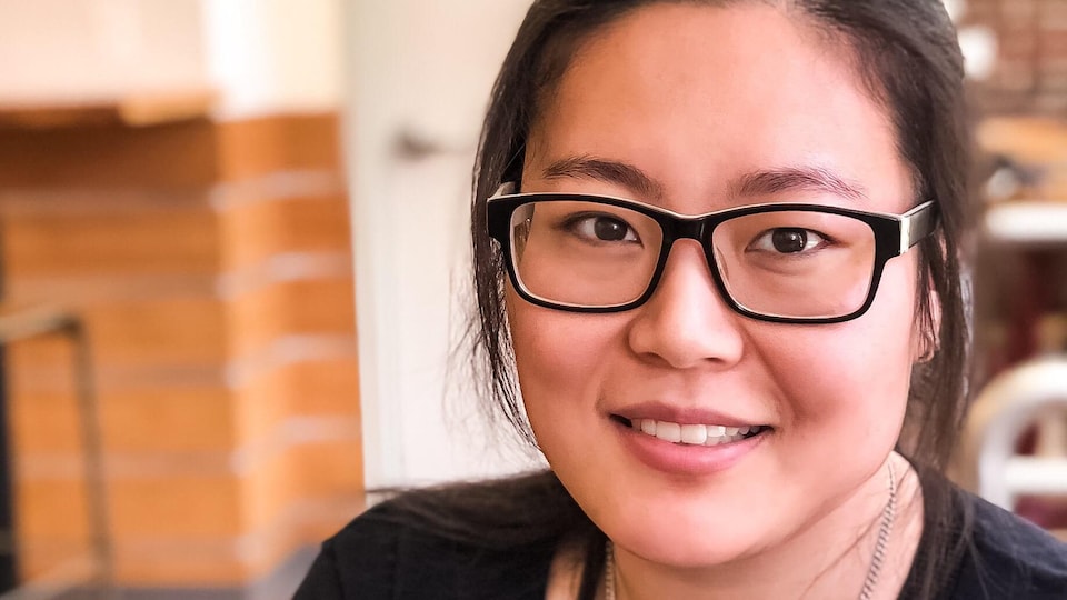 Une jeune femme d'origine asiatique souriante qui porte des lunettes.