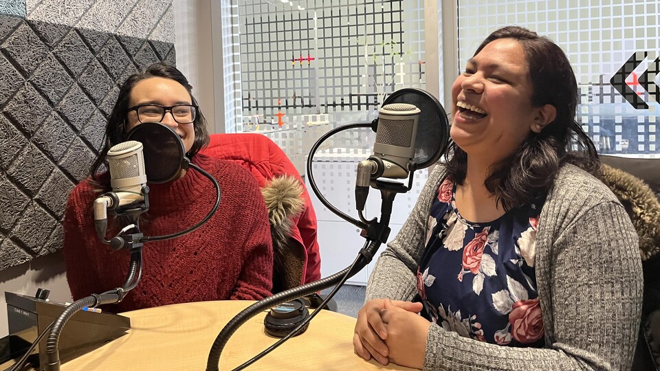 Deux femmes vêtues de couleurs vives et bigarrées rient dans un studio de radio