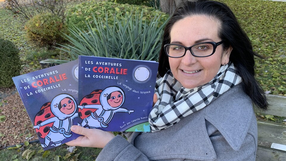 Une femme souriante, portant des lunettes, tient deux livres pour enfants dans ses mains