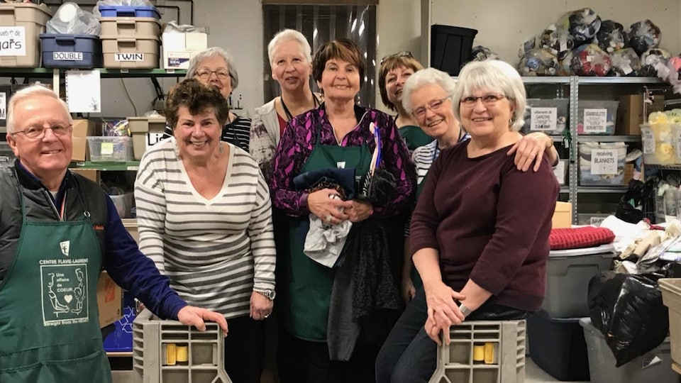 Un groupe de huit personnes dans une salle pleine de sacs et de boîtes de dons