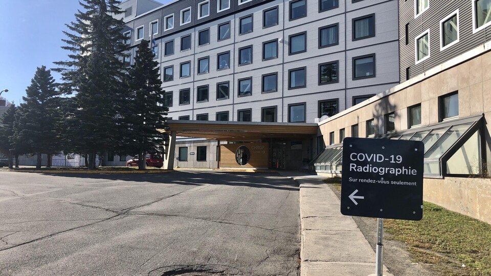 Un hôpital avec un écriteau à l'avant-plan indiquant le secteur désigné à la COVID-19.