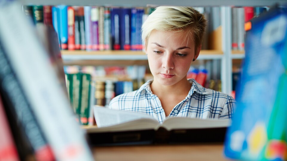 Une adolescente lit un livre dans une bibliothèque.