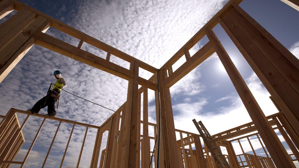 Un travailleur debout sur la structure d'une maison en construction.