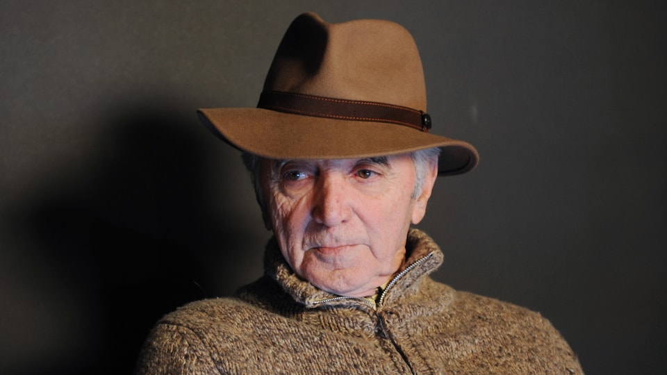 Charles Aznavour, chapeau de feutre sur la tête, le regard dans le vide.