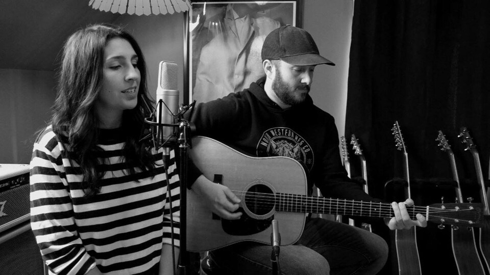 Photo en noir et blanc de Monique Comeau, au micro, et Charles Robichaud, à la guitare.