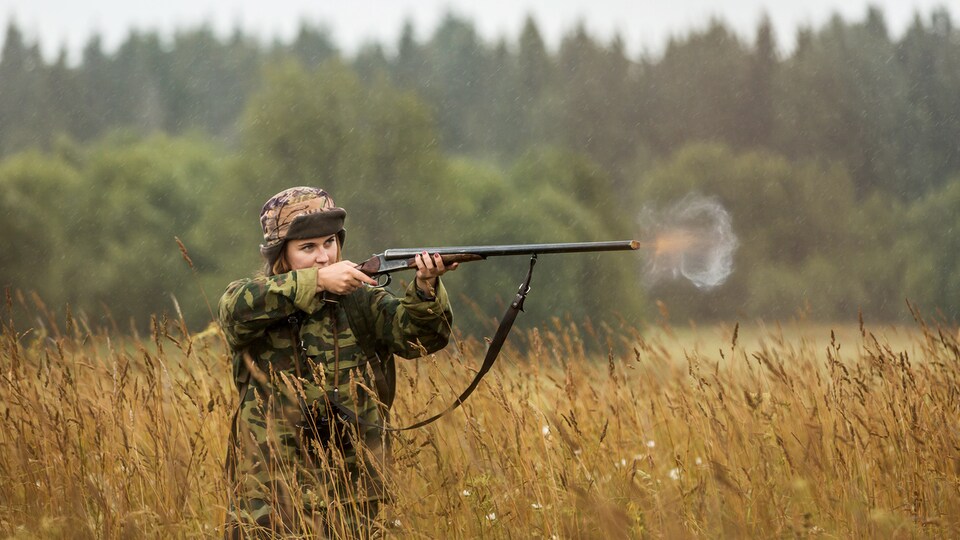 Une femme habillée en tenue de camouflage tire un coup de sa carabine.