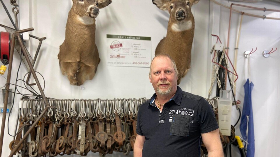 Un homme pose devant du matériel de boucher et deux têtes de chevreuil.