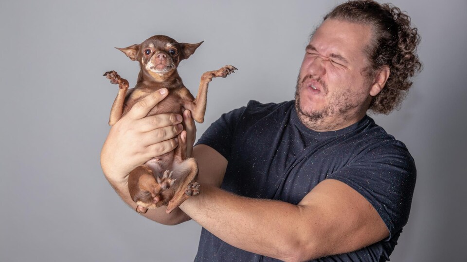 Un homme a une moue de dégoût en tenant un petit chien au bout de ses bras.