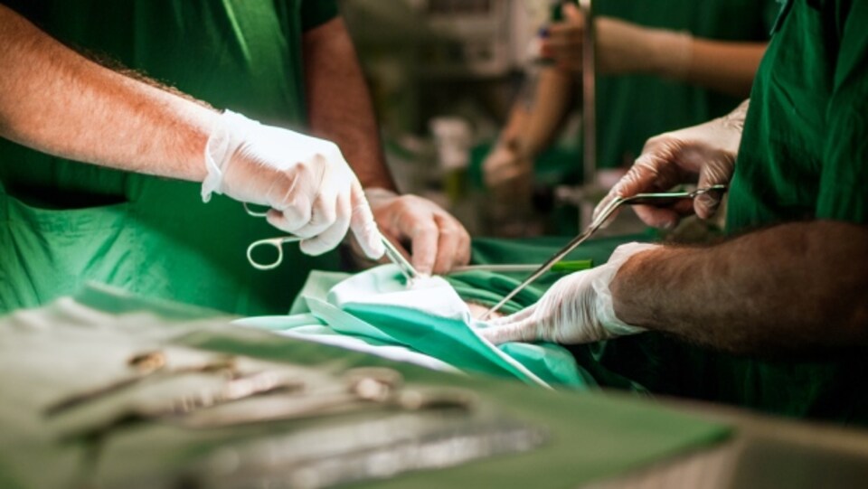 Gros plan sur les mains gantées de deux chirurgiens, qui opèrent un patient.