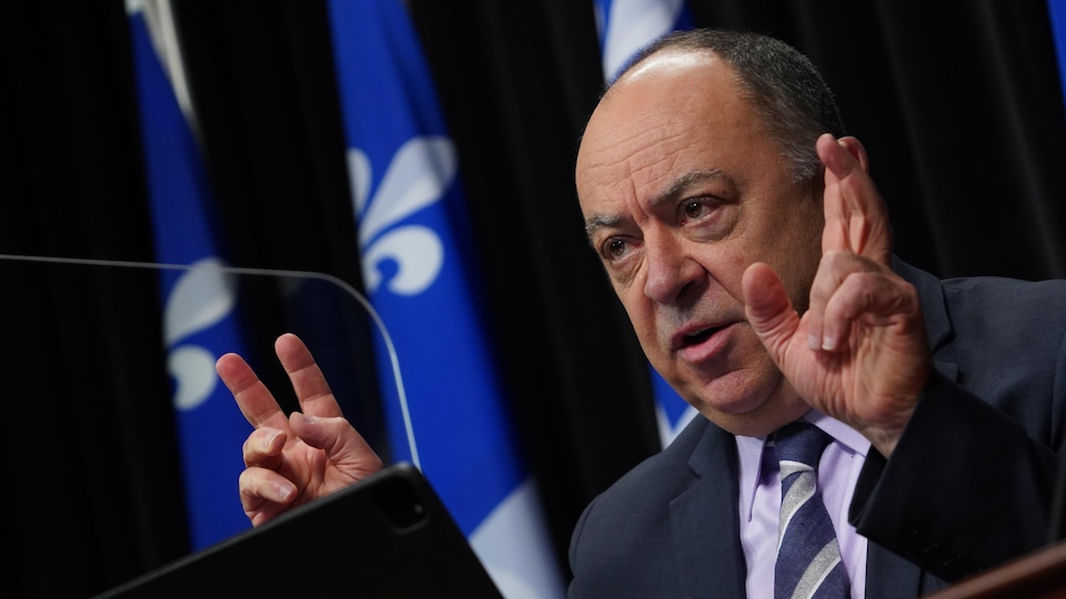 Christian Dubé s’adresse aux médias assis à la table de presse. 