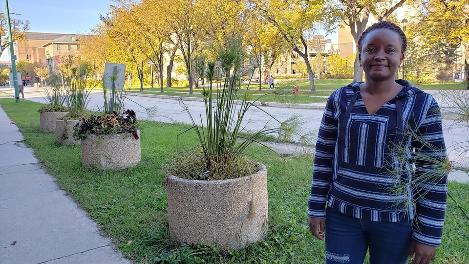 La Christianne Dunia est debout près de fleurs et avec des arbres aux couleurs d'automne derrière elle.