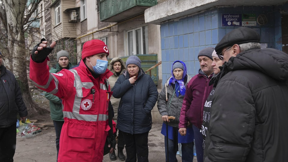 Des gens discutent avec un employé de la Croix-Rouge à côté d'un immeuble à Marioupol, en Ukraine, le 7 mars 2022. 