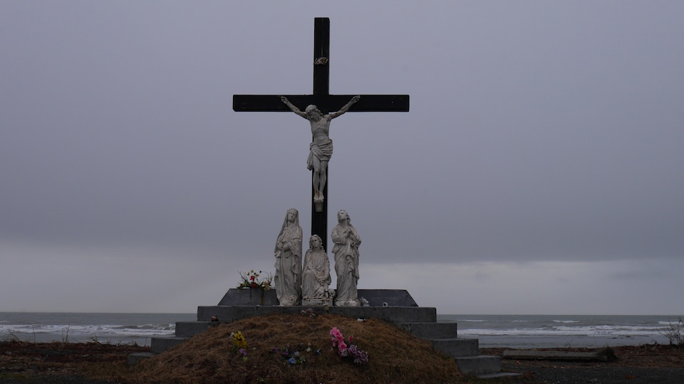 Une grande croix avec une statue de Jésus-Christ dessus au centre d'un petit cimetière.