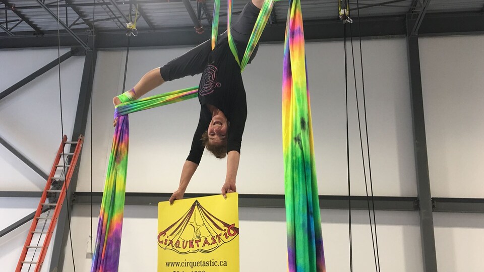 Lyne Gosselin accrochée la tête en bas sur des rubans tient une affiche du Cirquetastic.