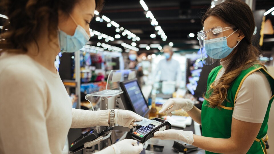 Une caissière fait payer une cliente dans une épicerie.
