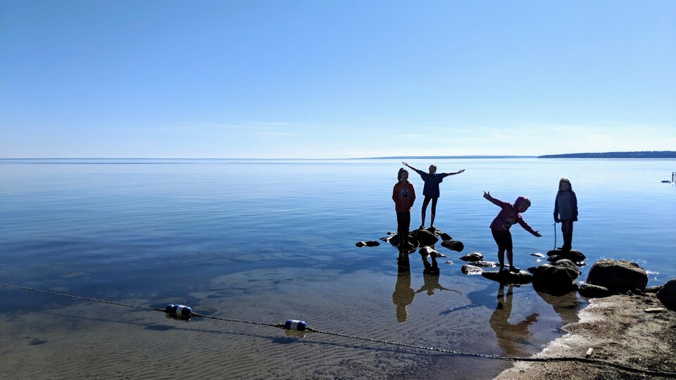 Des enfants debouts sur des pierres dans un grand lac.