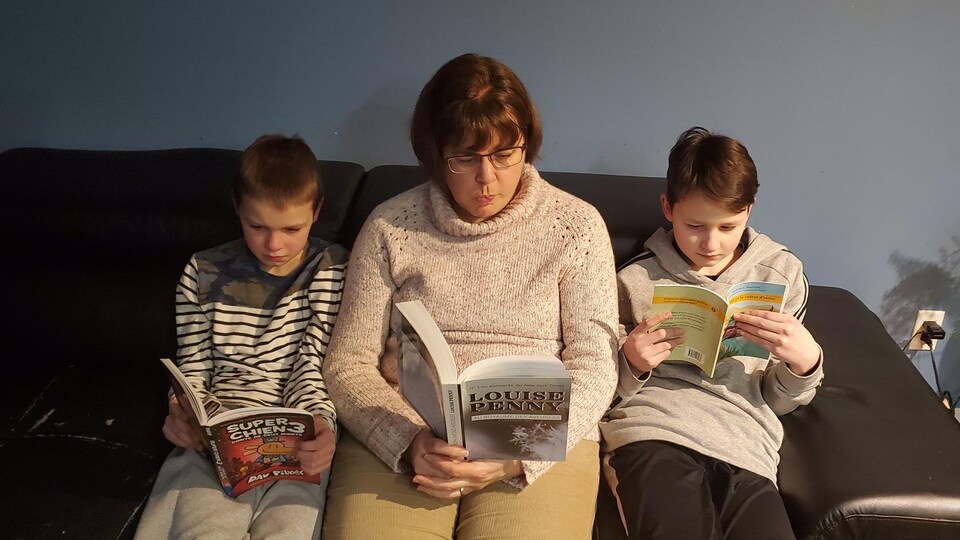 une dame et deux enfants assis sur un canapé, un livre à la main.