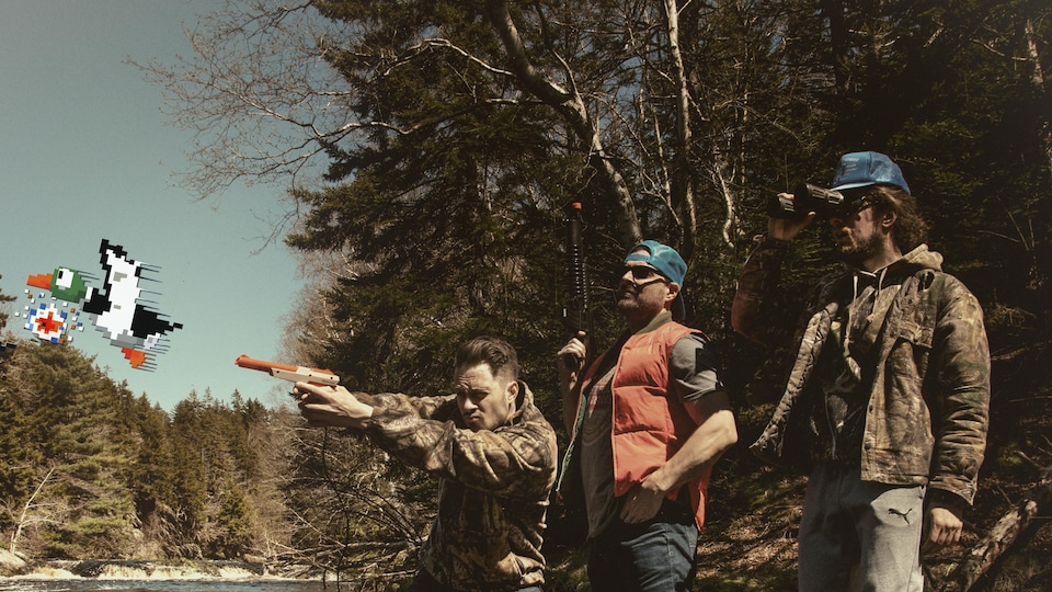 Jean-Pascal Comeau, Daniel Leblanc et Arthur Comeau, habillés en chasseurs, les pieds dans une rivière, avec un chien à leurs côtés. Jean-Pascal Comeau tient un pistolet de Nintendo orange NES Zapper, la version de 1989, et fait semblant de tirer sur le canard du jeu Duck Hunt, ajouté à la photo.