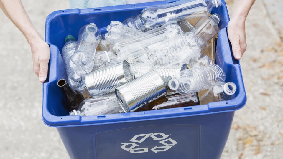Quelqu'un tient un bac de recyclage bleu rempli de bouteilles de plastique vides.