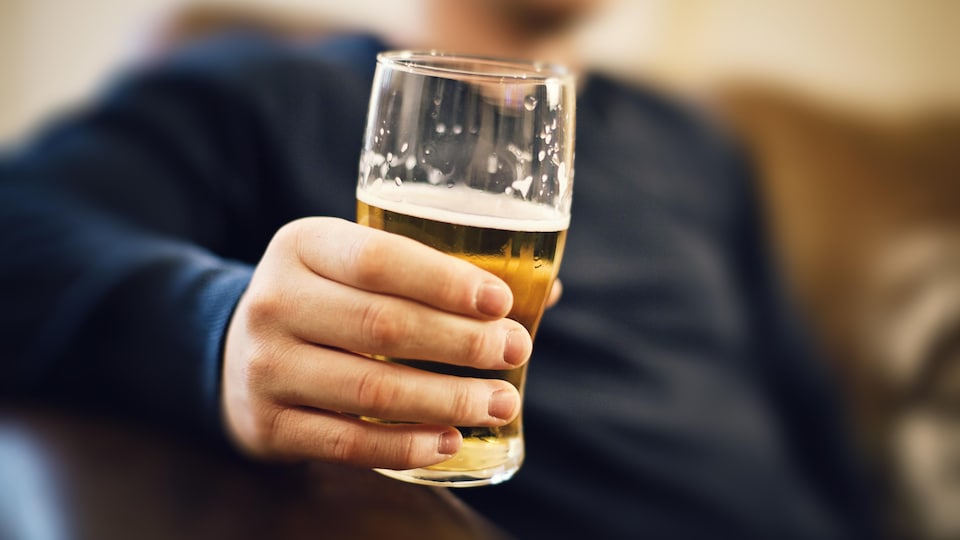Gros plan sur la main d'un homme assis dans un divan qui tient une bière. 