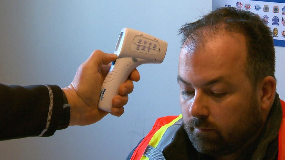 Un travailleur de la construction se fait prendre la température avec un thermomètre à distance en raison de la pandémie de COVID-19.